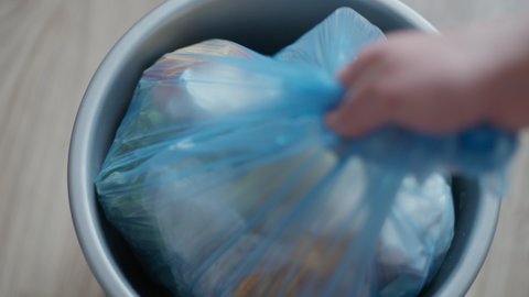Male hands gathering plastic bag with food waste in kitchen at home. Close-up unrecognizable Caucasian young man cleaning appartment leaving with litter