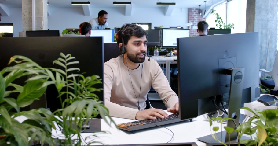 Arab handsome man in headset working at computer screen and talking with client online. Customer support. Male talking in headphones at call center office. Developer worker speaking with customers. Royalty-Free Stock Footage #1089255225