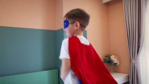 Child boy in red and blue Superman costume,little boy superhero, jumping in room on bed,in children's room.Superheroes, kid brother, play at home imagining they are superheroes.