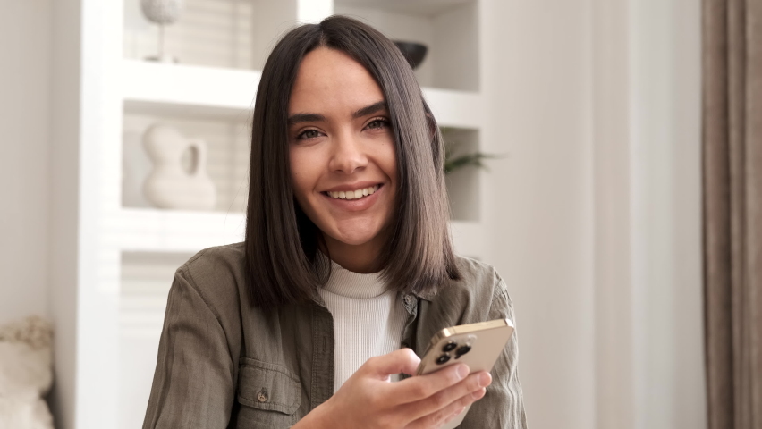 Happy woman smiling looking at camera. Home office interior. Business woman closeup portrait. Girl using smartphone internet surfing communication online. Pretty woman holding phone. Slow motion  Royalty-Free Stock Footage #1089255457