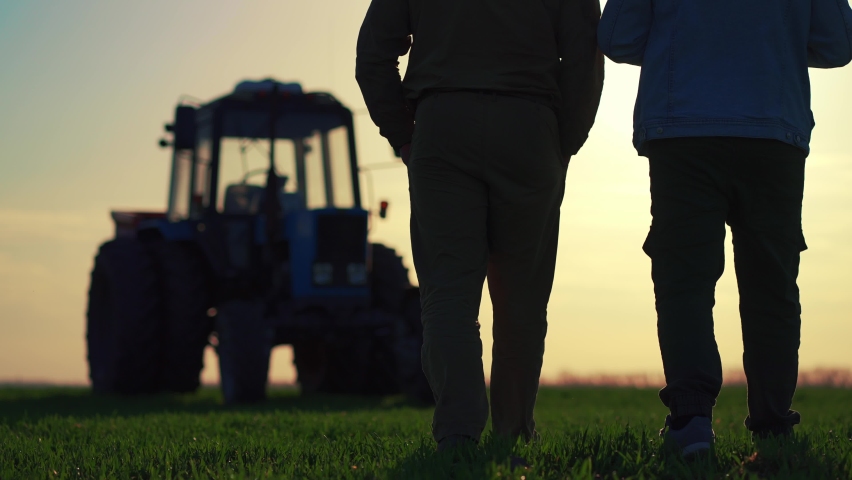 Teamwork concept. Silhouette two male farmers walking in a green field against sunset. Team farmers stand in a field on the background of agricultural machinery. Agronomists discuss harvest. | Shutterstock HD Video #1089257503