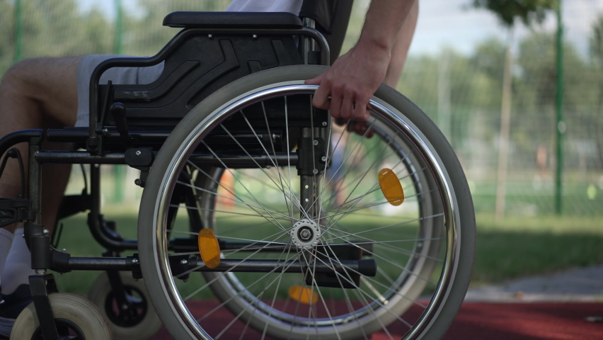 Side view male hands rolling wheelchair wheels riding fast in sunshine outdoors. Unrecognizable young Caucasian man riding mobility aid device training in park. Adaptive sport concept | Shutterstock HD Video #1089261201