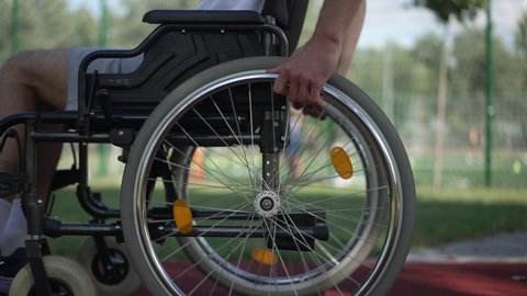 Side view male hands rolling wheelchair wheels riding fast in sunshine outdoors. Unrecognizable young Caucasian man riding mobility aid device training in park. Adaptive sport concept Stock Video