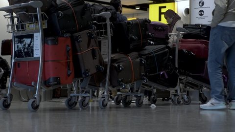 London , United Kingdom (UK) - 03 19 2022: Row Of Packed Suitcases On Luggage Trolleys At Heathrow Airport. Low Angle, Locked Off