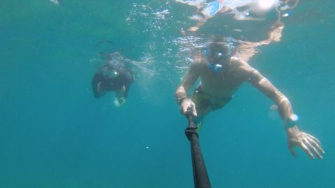 Selfie of a young couple swimming underwater in a tropical lagoon. Two people have fun with an underwater camera while filming their vacation. Slow motion