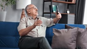 Modern elderly man talking online video call use smartphone remotely communication with relatives family. Male grandfather patient calling doctor medical service on mobile phone sitting on couch home
