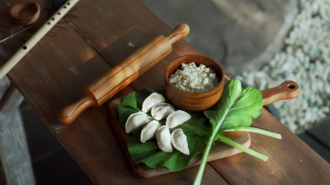 Traditional rustic Russian fresh handmade dumplings lying on a wooden table on a cutting board with cottage cheese in a wooden plate and spinach