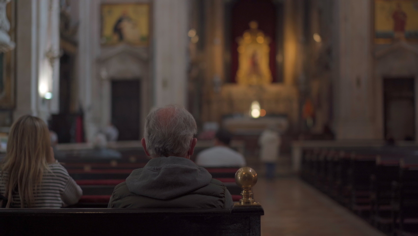 Elderly man prays while sitting on bench inside church, rear view. Catholic Church inside evening prayer, dark mystic atmosphere Man sitting pew at Church and meditating, faith and religion concept | Shutterstock HD Video #1089274507