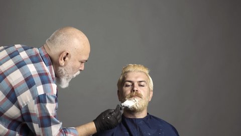 Bearded man coloring hair. Stylist with hair dye and brush coloring hair at salon. Hair coloring man.