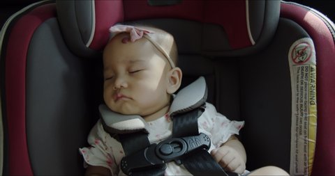 Close up - cute Asian baby girl sleeping in a car seat. Slow motion of toddler travelling in driving car. Child’s passenger safety product in family road trip concept. 