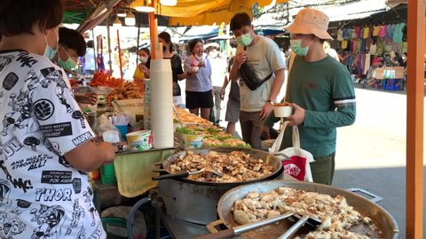 BANGKOK, THAILAND - Circa November, 2021: Chef is preparing yummy cuttlefish for customers at Chatuchak Weekend market, Thailand's famous tourist attraction. Point of view shot people shopping 