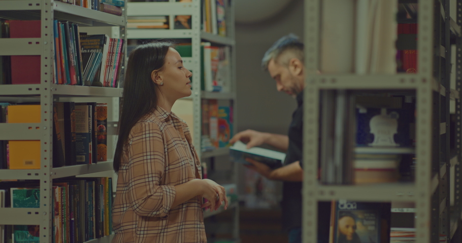 Young woman and man take books from the shelves of the library, shelves with bookshelves. Enthusiastic readers open books and look into them with interest, the reading room of the scientific library