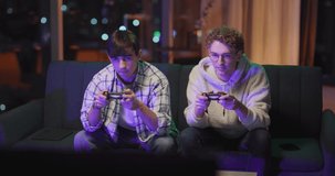 Couple of handsome caucasian college young boy students playing video games on console joystick devidces ending up in draw doing high-five.