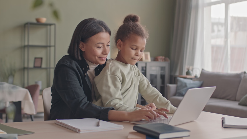 Medium slowmo of young Biracial woman embracing her pretty 8 year old daughter watching videos on laptop together staying at home during lockdown Royalty-Free Stock Footage #1089284689