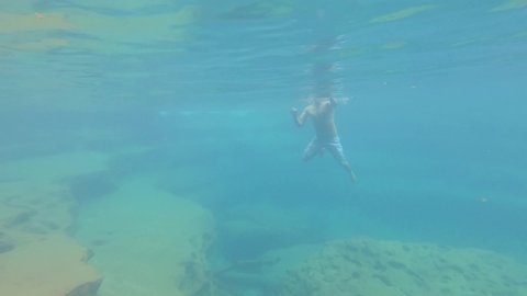 young man swimming in blue crystal clear under water of waterfall from top angle