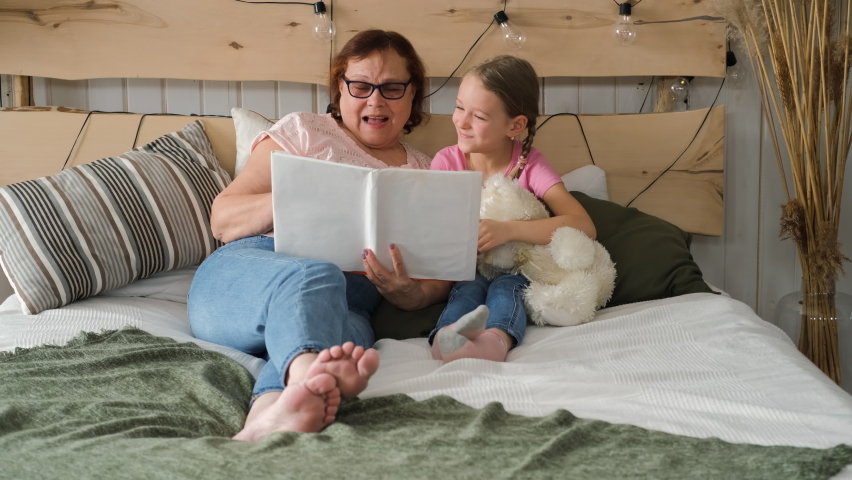Little Girl with Grandmother Having Fun while Reading Book in Bed. Happy Family and Generation Concept Royalty-Free Stock Footage #1089287835