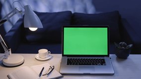 Close up zooming shot of modern chroma key green screen laptop computer set up for work on desk at night. Remote work, technology concept 4k uhd video template.