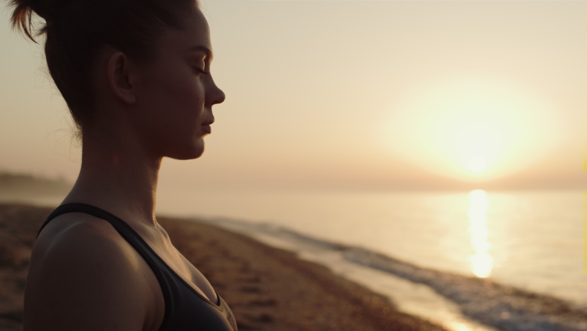 Profile of sportswoman making meditation exercise on beach cposeup. Attractive girl closing eyes practicing yoga asana at sunrise. Focused woman sitting on sand enjoying nature energy. Harmony concept | Shutterstock HD Video #1089289763