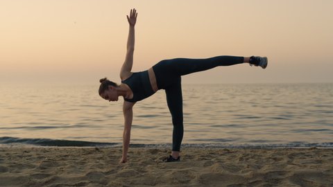Athlete girl making ardha chandrasana standing sandy beach at twilight. Yoga woman practicing half moon pose near calm sea. Sporty lady stretching training balance in front evening sky. Healthy sport.