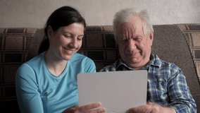 Woman daughter helps elderly old man to communicate on video call communication to Internet with relatives, friends and doctor. Caring for pensioners, teaching grandfather modern technologies.