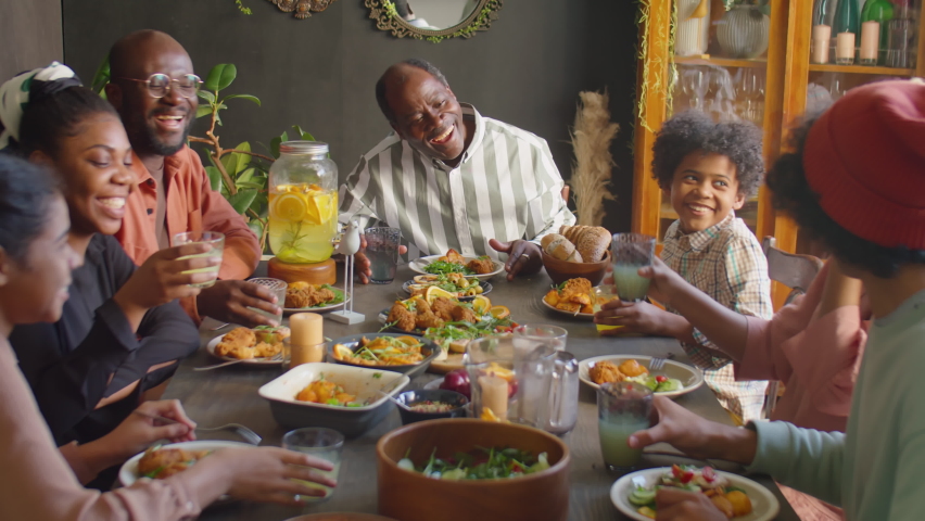 Big African American family clinking glasses in toast, drinking lemonade and eating meal while having holiday dinner at home