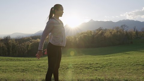 Young woman squats workout. Beautiful fitness model workout outdoors. Sunset with mountains in background.