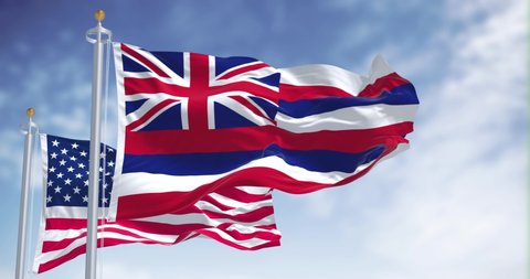 The Hawaii state flag waving along with the national flag of the United States of America. In the background there is a clear sky. Hawaii is a western state of the United States. Slow motion in 4k res