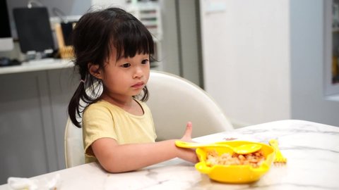 Asian little girl child sit at dinner table so full and bored while eating their own fried rice with a yellow shirt and yellow plate set of spoon and fork.