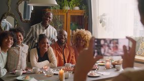 Large African American family smiling and posing together on camera at home holiday dinner while kid taking picture with smartphone - Powered by Shutterstock - Get 15% off with code: PIKWIZARD15