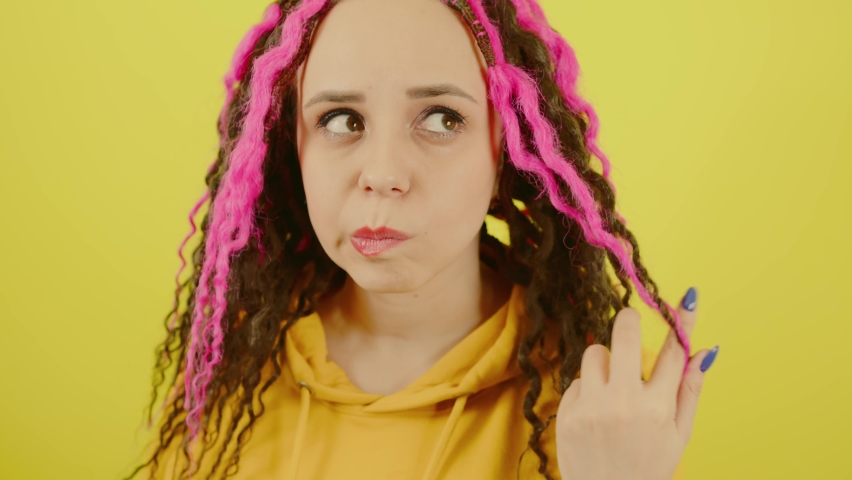 Young woman twists hair with thoughtful look on yellow background. Beautiful female with curly hair looking away and reflecting on life.