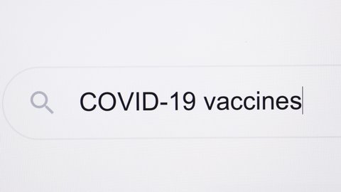Typing the word COVID 19 vaccines in the browser and clicking the search button on a pixelated computer screen. COVID-19 vaccines - Internet browser search bar typing coronavirus information research.