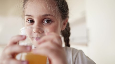 girl child drinking juice. happy family a healthy eating kid dream concept. daughter girl drinking yellow juice indoors from a glass cup in the kitchen. child drinking fruit juice