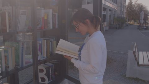 Teenage girl leafs through a book while traveling. Ways of replenishment of the vocabulary. Free public library books sharing box. CH, Zurich, 13.3.22