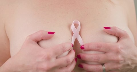 Closeup Topless Woman's Hands Covering Her Breasts With Pink Ribbon Placed At The Middle. Breast Cancer Awareness Concept. - Closeup Shot