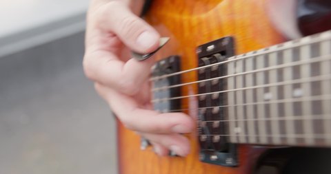 Camera shoots video the fretboard of an electric guitar, at the end the musician plays a chord with a mediator. Human hands playing on electric guitar. Fingers on guitar strings.