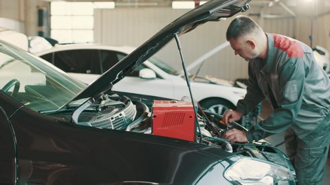 Auto mechanic working on car diagnostic in a repair shop. Electrician working on car engine. Mechanic repairs car in a car repair station. Testing electrical system on automobile.