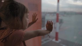 Little girl at the airport is waiting for landing at the big window. Cute kid stands at the window against the backdrop of airplanes. Looking forward to leaving for a family summer vacation - Powered by Shutterstock - Get 15% off with code: PIKWIZARD15