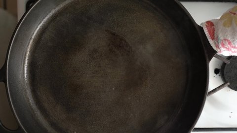 Placing a raw steak into a hot cast iron skillet with oil - Overhead view