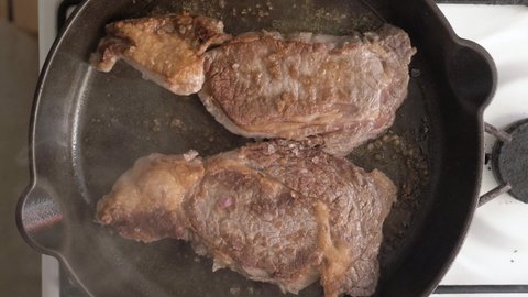 Steaks fried and flipped in a cast iron skillet with oil - Overhead view
