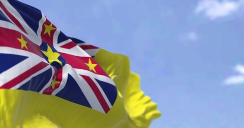 Close-up view of Niue state national flag waving in the wind. In the background there is a clear sky. Niue is an island state in the South Pacific Ocean. Selective focus. Seamless loop in slow motion