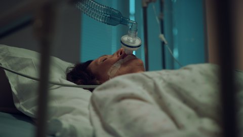 Sick woman wearing oxygen mask portrait. Terminally ill person lying in ward. Aged female attached to artificial breathing device clinic intensive care unit. Unconscious aged patient in coma concept.