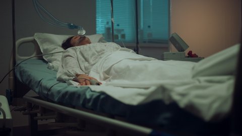 Patient connected artificial breathing tubes in hospital intensive care unit. Unconscious woman with oxygen mask undergoing covid treatment in modern clinic. Sick female in coma lying resting in bed.