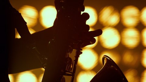 Musician hands playing saxophone professionally in jazz club close up. Unrecognizable virtuoso saxophonist performing on stage spotlights. Silhouette of player arms holding sax in nightclub lights.