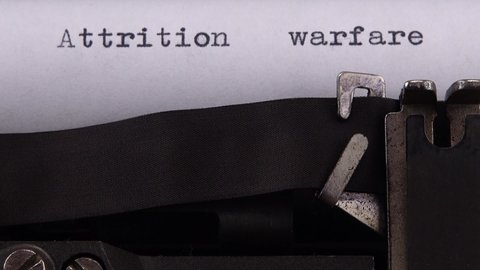 Typing phrase "Attrition warfare" on retro typewriter.