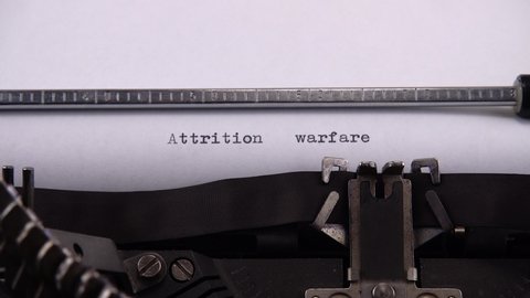 Typing phrase "Attrition warfare" on retro typewriter.