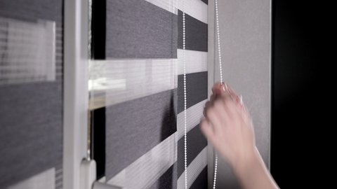 Woman hands pulling string as blinds drop window roller duo system day and night. Close up on roll curtains indoor