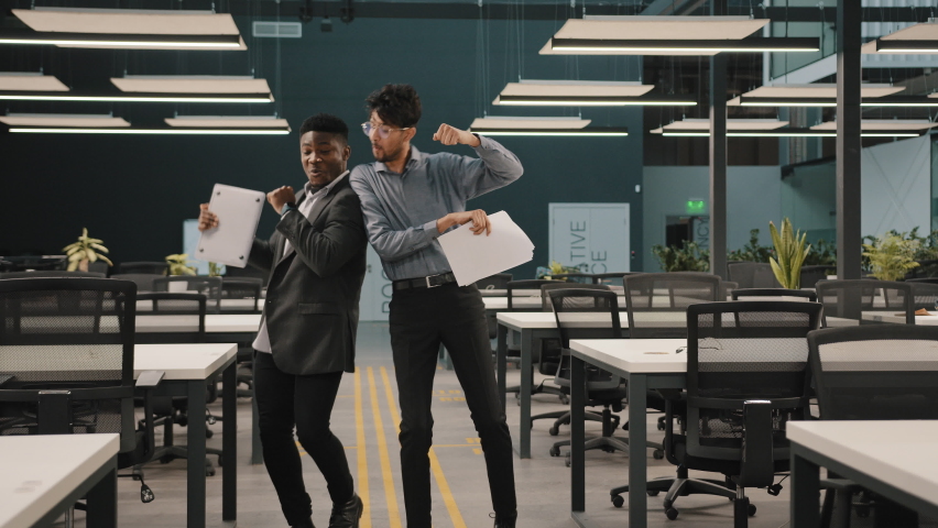 Overjoyed Arab professional male worker African man employee dancing in office background celebrating achievement with dance move motivated business partner enjoying sucess negotiation victory concept