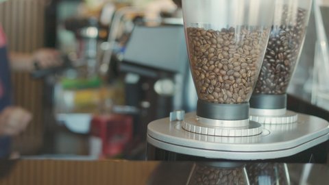 Close up shot with copy space of coffee beans in dispenser machine placing on table top in coffee shop with blur background of coffee preparation by barista for background of beverage business.