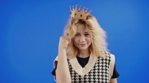 Funny Looking Young Blonde Woman Wearing A Royal Paper Crown Isolated Against Blue Studio Background. - Medium Shot