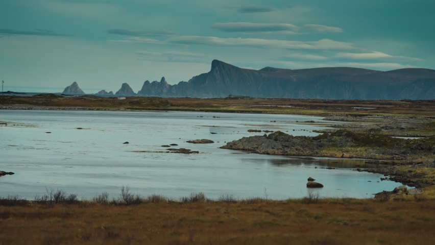 Shallows and swampy shores of the Andoya island. Heavy clouds cover the sky. Misty mountains in a distance. Slow-motion, pan follow.